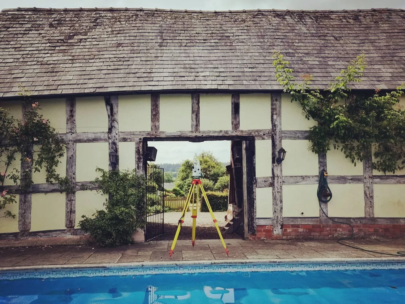 Total station set up in the open doorway of a timber-framed barn beside a swimming pool
